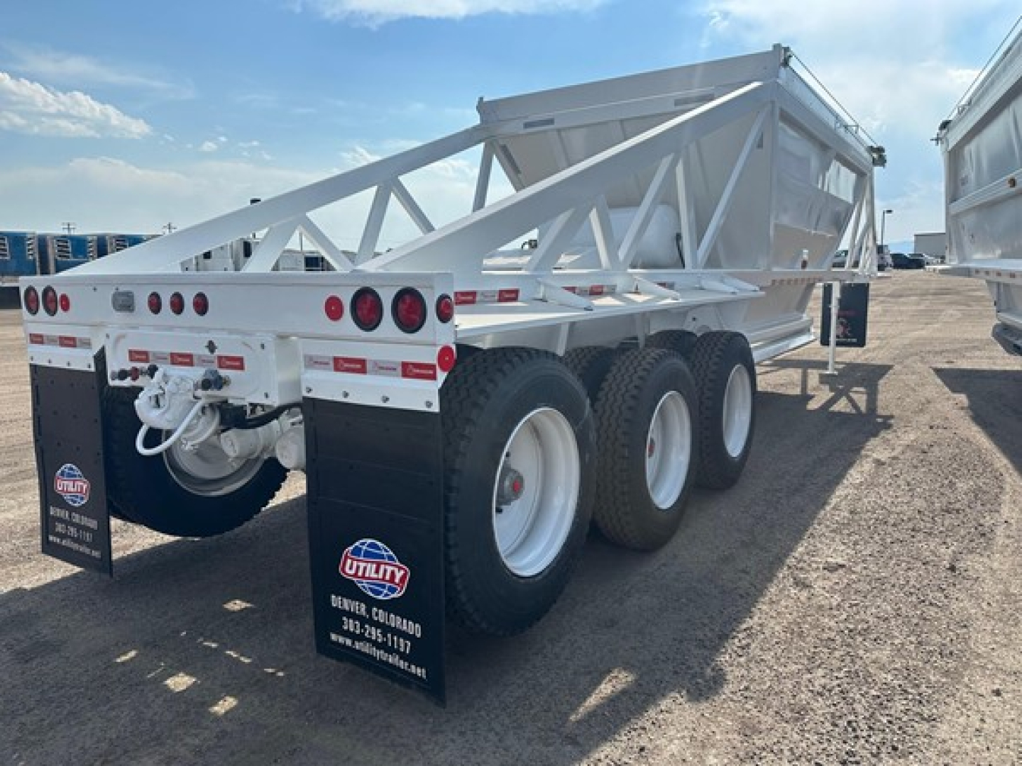 Tri-axle bottom dump trailer showing white frame, wheels, and rear lights; mud flaps display Utility trailer logos and Denver, Colorado contact info.