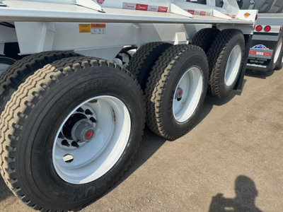 Bottom dump trailer with tri-axle configuration showing three rear wheels and white rims; treaded tires and suspension visible.