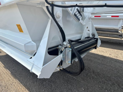 Bottom-dump trailer hitch and hydraulic line assembly on white Ranco tri-axle dump trailer rear corner view.