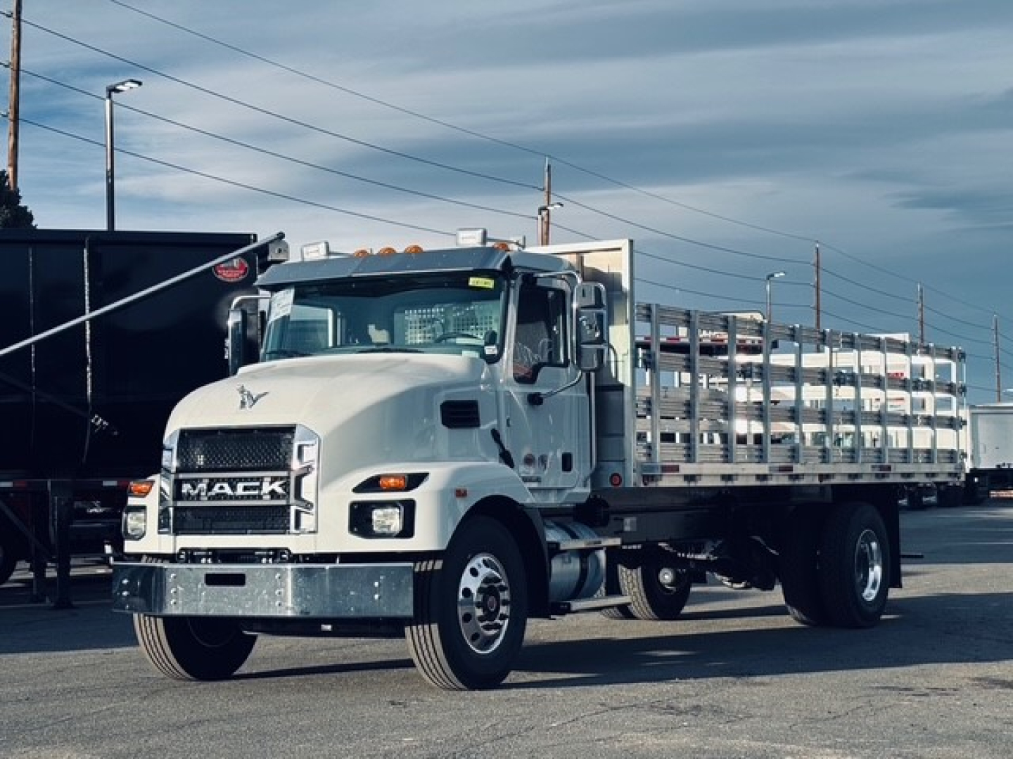 Mack MD7 truck in a flatbed configuration with a chrome front bumper, large grille, and a high cab; mud flaps and stacked side rails visible along the flatbed.