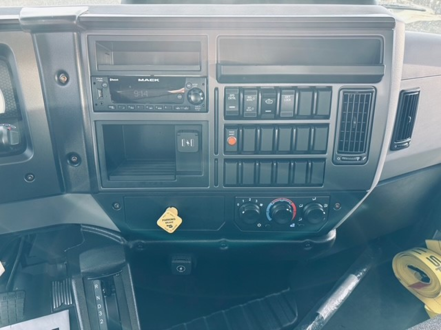 Mack MD7 truck dashboard with radio, climate controls, and multiple switches; some text on dashboard includes ‘MACK’ on the radio face and labels on switches. Also visible are knobs and a yellow key tag.