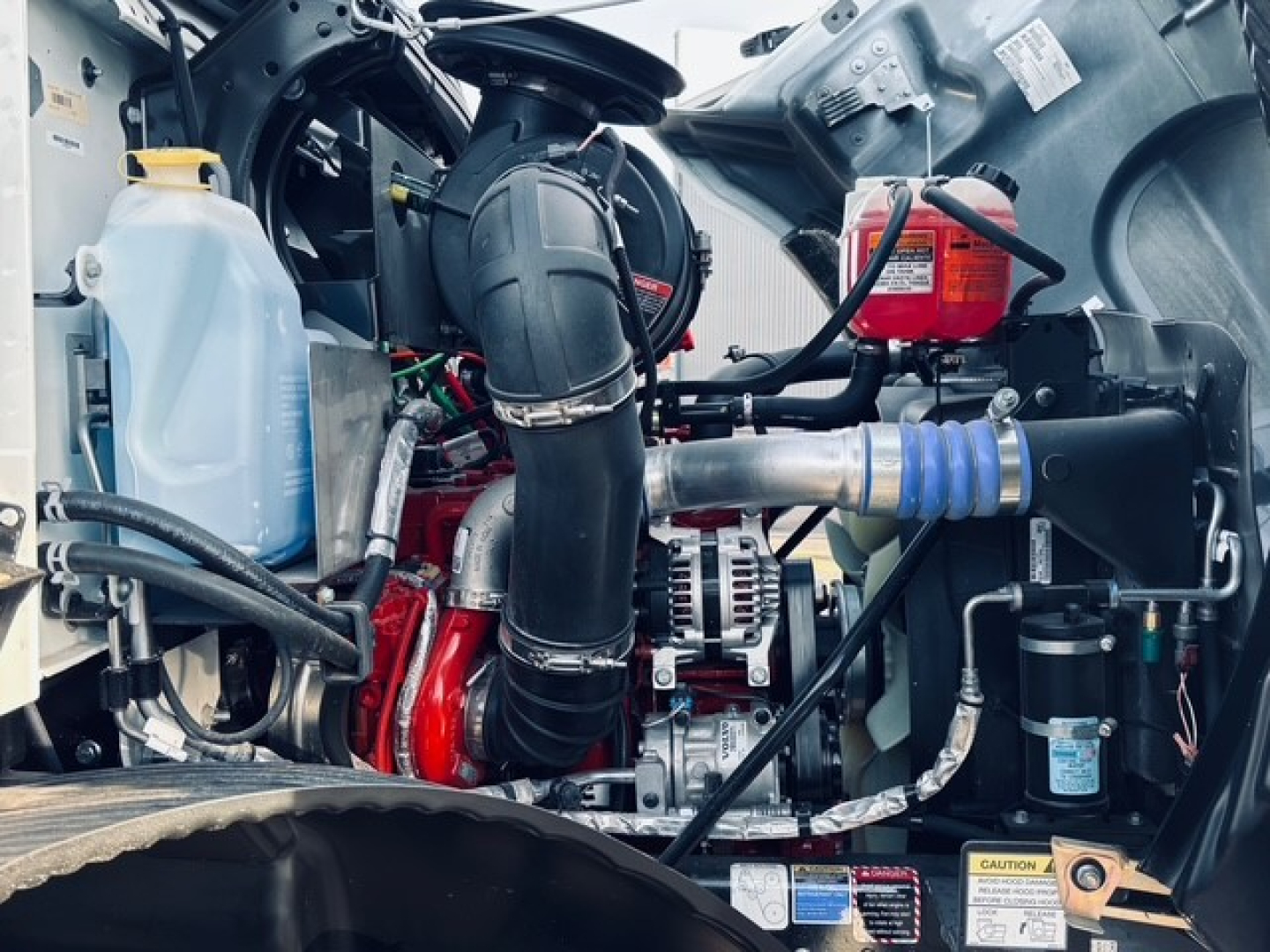 Mack MD7 engine bay showing air intake, coolant reservoir, alternator, hoses, and turbo piping.