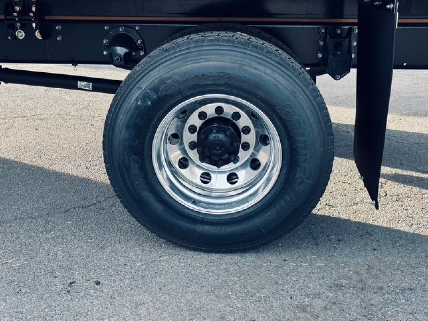 Wheel and tire showing steel rim on Mack MD7 flatbed truck chassis with black frame and suspension components.
