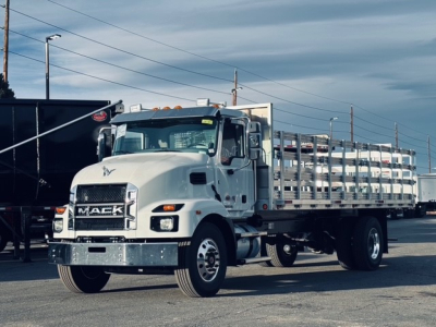 Mack MD7 truck in a flatbed configuration with a chrome front bumper, large grille, and a high cab; mud flaps and stacked side rails visible along the flatbed.