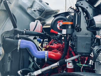 Mack MD7 engine bay view showing blue coolant hose, red intake manifold, black wiring harness, pink reservoir, and various engine components.