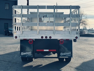 Mack MD7 truck rear view with flatbed and aluminum side gates, taillight cluster, mud flaps labeled Brackner's Equipment, and rear bumper on a paved lot.