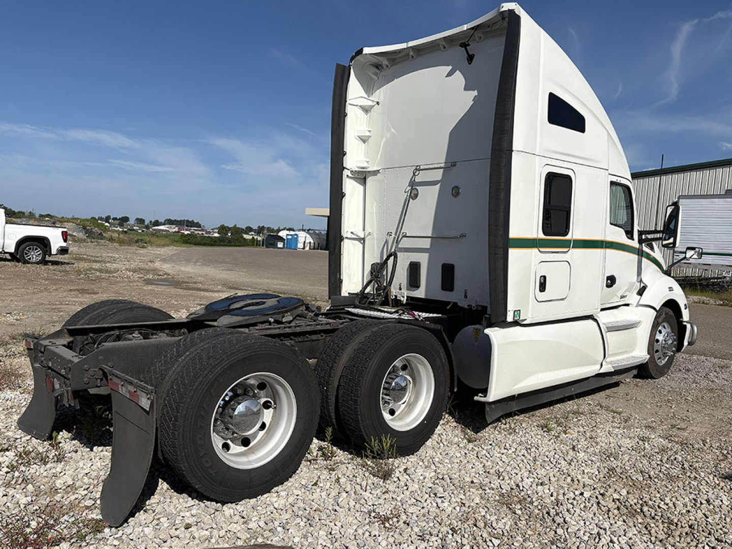 Kenworth T680 tractor truck in a lot showing the rear section and cab with white paint and green/yellow stripe; visible wheel rims and fifth wheel; no readable small text.