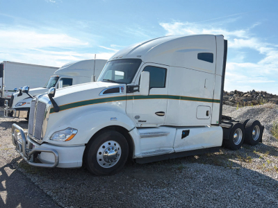 Kenworth T680 tractor unit in white with green and gold stripe, side profile, sleeper cab, three rear axles, visible front grille guard.