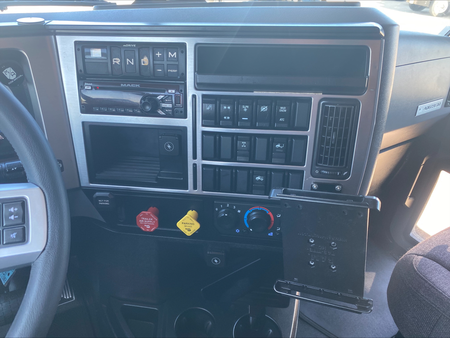 Truck dashboard interior showing gear selector area with buttons, climate controls, and radio slots in a Mack AN64T70 cab.