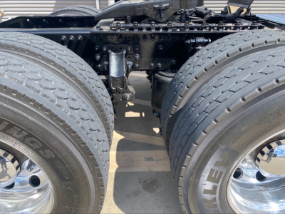 Truck axle area showing dual rear tandem wheels and suspension components, with large MACK oil/air lines and frame rails visible.