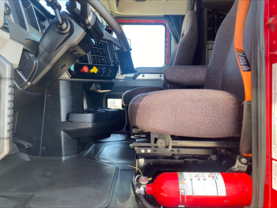 Cab interior of a 2020 Mack AN64T70 truck showing driver seat and dashboard with controls and a red fire extinguisher visible under the seat.