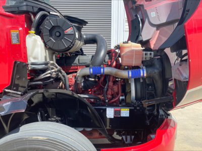 Mack AN64T70 engine bay showing radiator, hoses, coolant reservoir, and air intake. Visible components include blower fan and engine block with blue hose clamps.