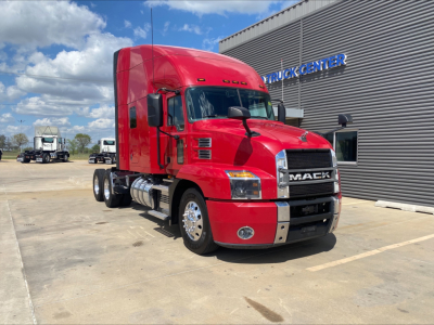 Red Mack tractor cab with sleeper showing front grille with 'MACK' logo, large side mirrors, and headlights in a dealership lot.