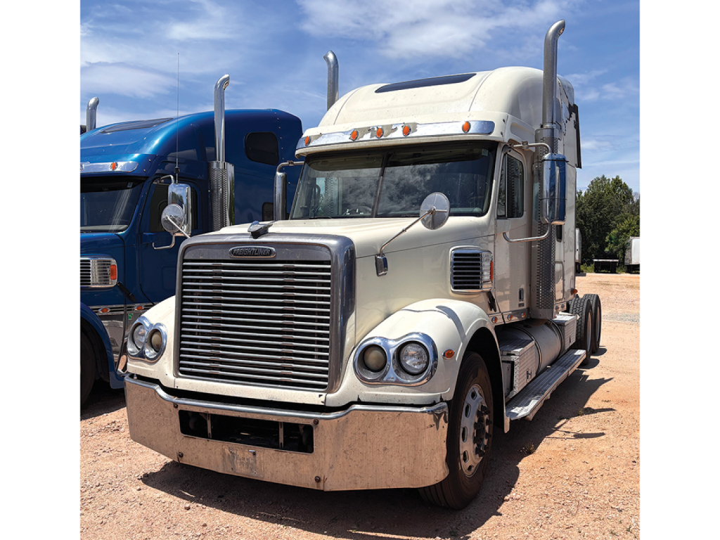 Freightliner Coronado sleeper tractor showing chrome grille, dual round headlights, beige paint, and tall exhaust stacks.