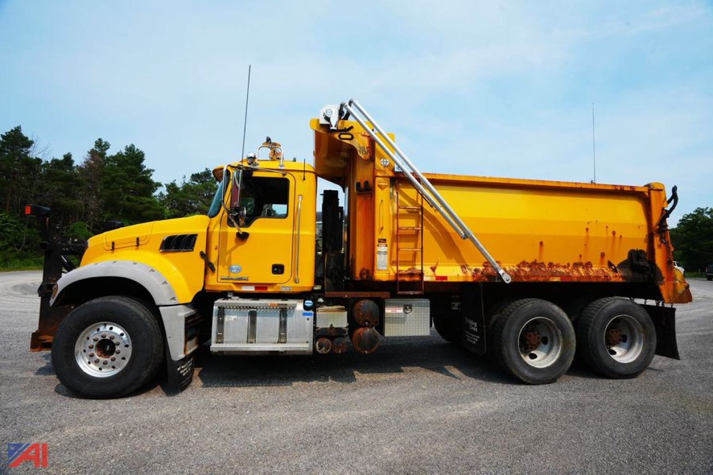 Dump truck side view showing yellow Mack GU713 with plow and dump bed, chrome steps, and dual rear axles.