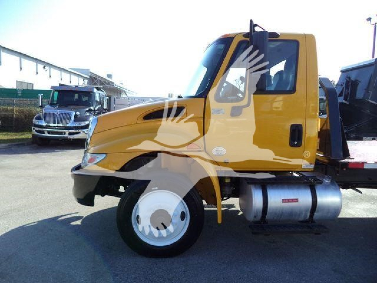Truck cab of a yellow 2019 International 4300 auto carrier side view showing front wheel and fuel tank.