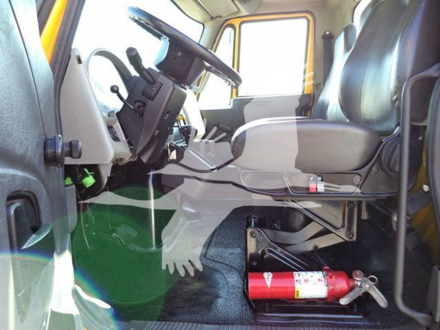 Cab interior of a 2019 International 4300 auto carrier showing steering wheel, driver seat, dashboard, pedals, and a red fire extinguisher mounted under the seat area.