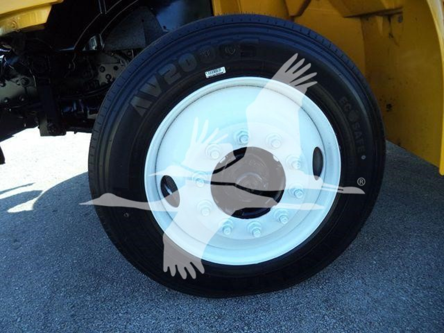 Tire on wheel showing wheel hub and part of yellow truck body; black tire with white rim mounted on vehicle.