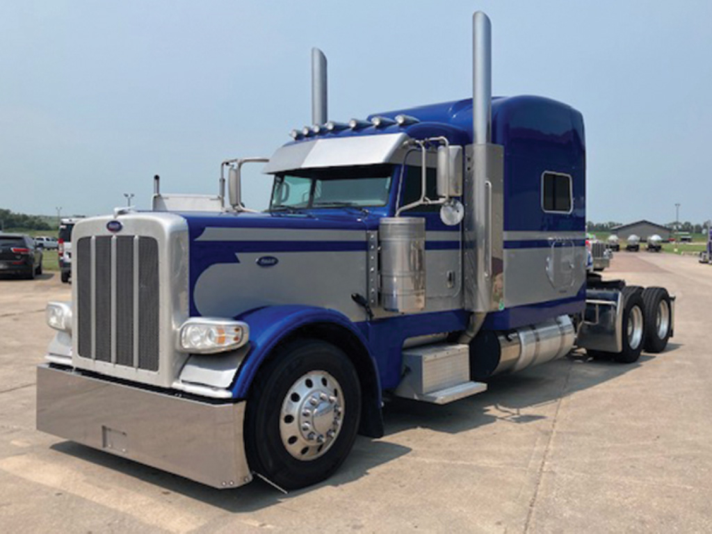 Peterbilt 389 UltraCab extended hood truck in blue with chrome accents and dual tall exhaust stacks; front chrome bumper and large grille.
