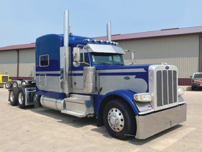 Blue and silver 2020 Peterbilt 389 UltraCab extended hood tractor, chrome front bumper, dual tall exhaust stacks, chrome fuel tanks, large grille, daytime running lights.
