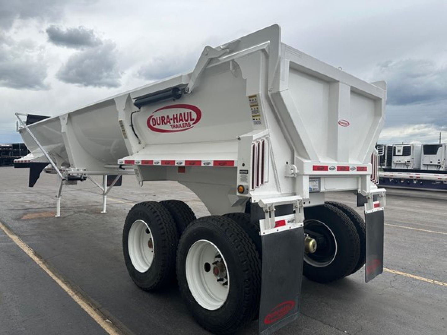 Dura-Haul frameless 1/2 round rock end dump trailer in a parking lot, white with red logo, dual rear wheels, mud flaps, side marker lights.