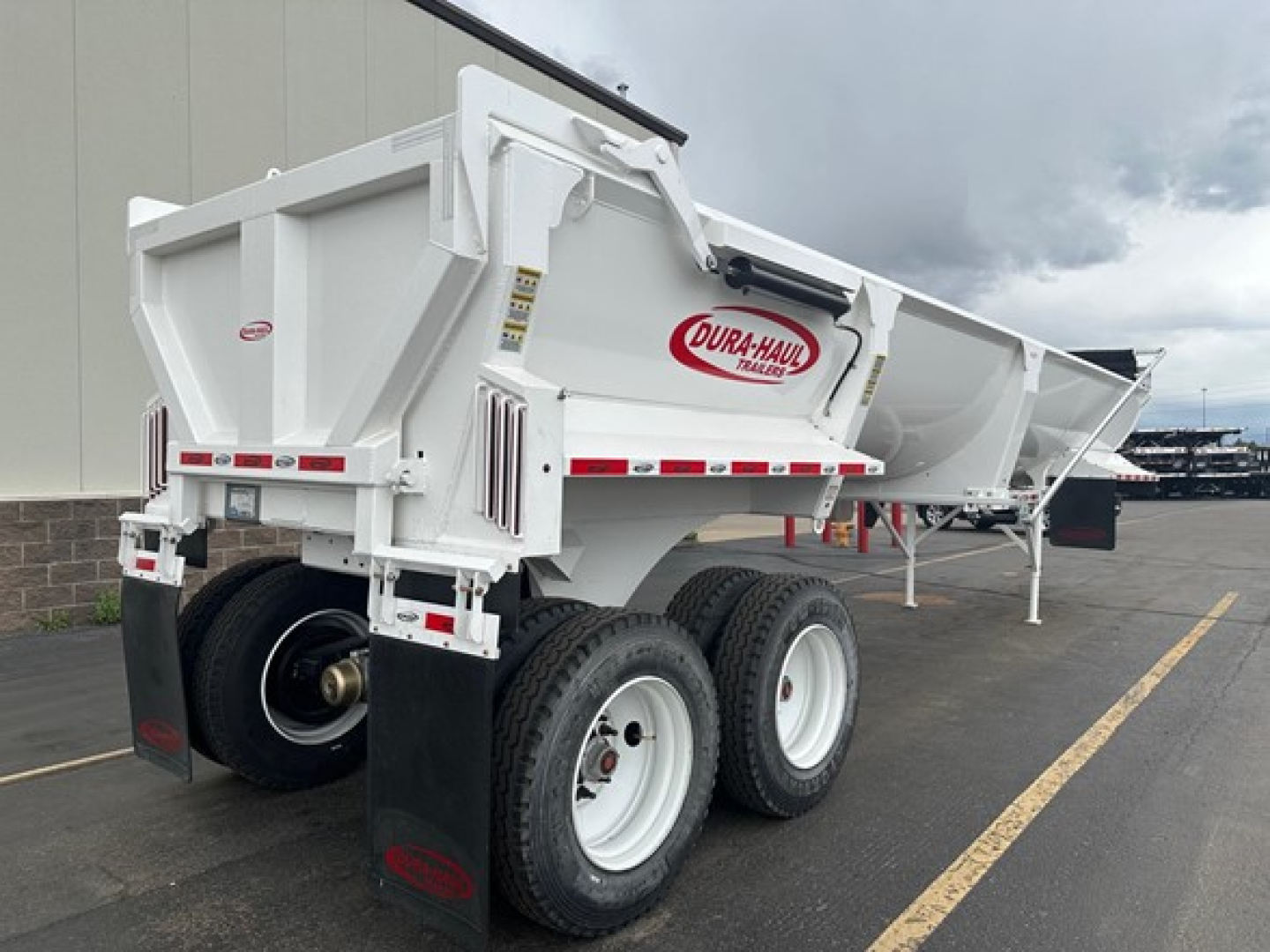 Dura-Haul frameless half-round rock end dump trailer with dual rear axles, white body, red logo, and black mud flaps.