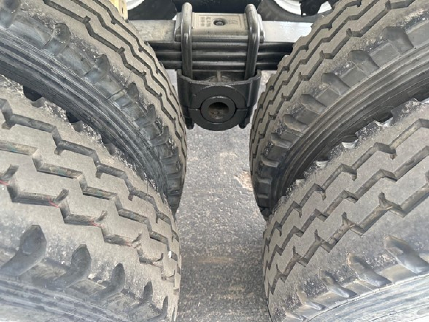 Trailer rear view showing dual axles and leaf spring suspension between wheels, heavy-duty tires, black chassis components visible.