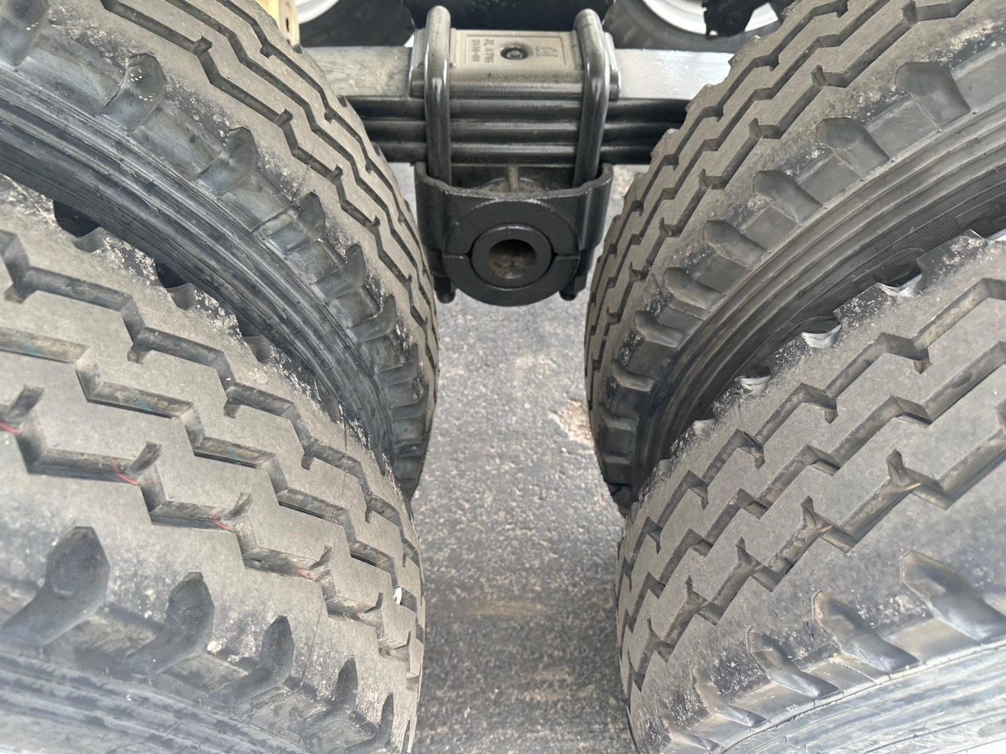 Trailer dual rear axles with heavy-duty tires and suspension showing the central pivot and leaf spring assembly.
