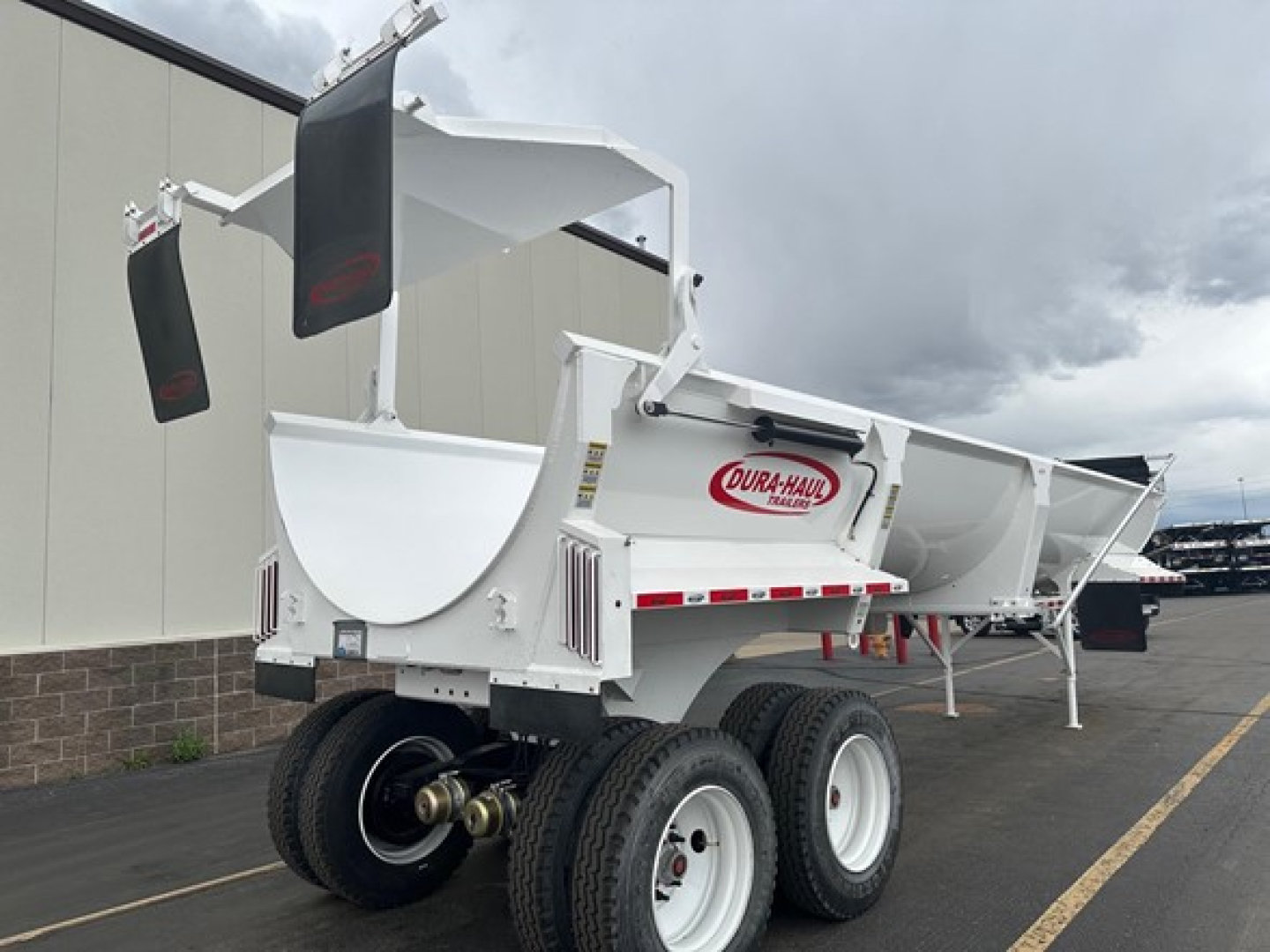 Frameless 1/2 round rock end dump trailer showing dual rear ladder braces and Dura-Haul logo on hopper, white finish, dual axles with heavy-duty tires.