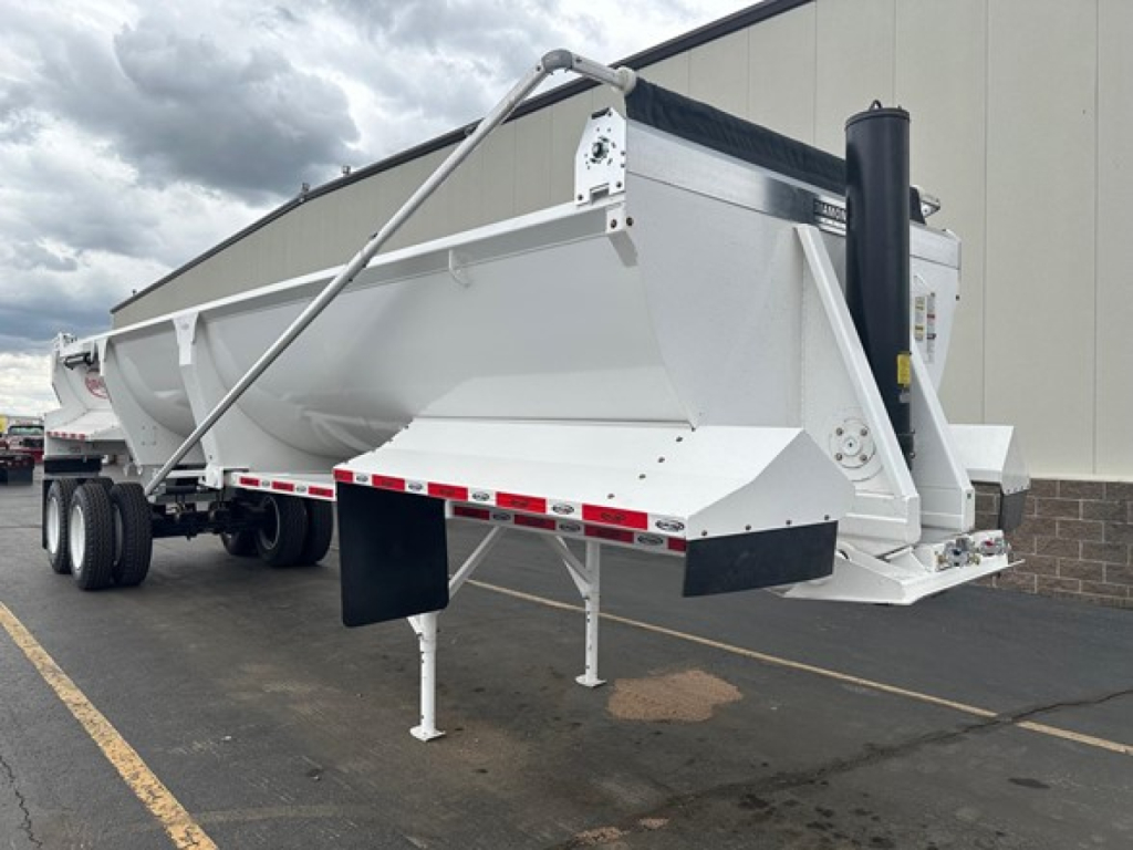 Trailer side view showing a Dura Haul frameless 1/2 round rock end dump with white body, black trim, and triple-axle rear; landing gear visible.