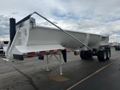 Frameless 1/2 round rock end dump trailer with high lift, white, side view showing front hitch and support legs.