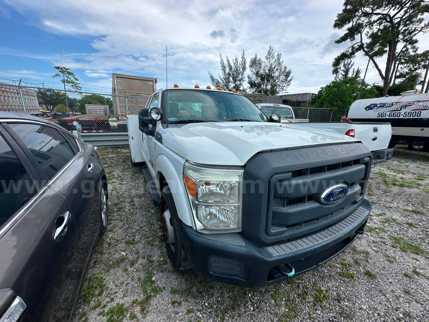 Ford F-350 service truck in a gravel lot showing front grille, headlights, and bumper with badge; white cab, black grille, utility truck features.