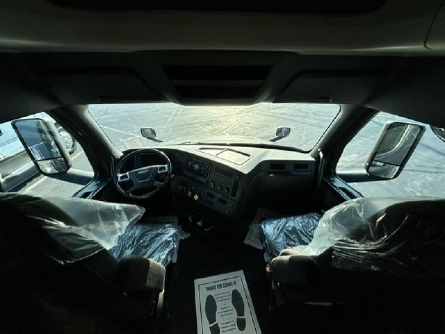 Cab interior of Freightliner Cascadia 126 conventional sleeper showing steering wheel, dashboard, and two front seats covered in plastic.