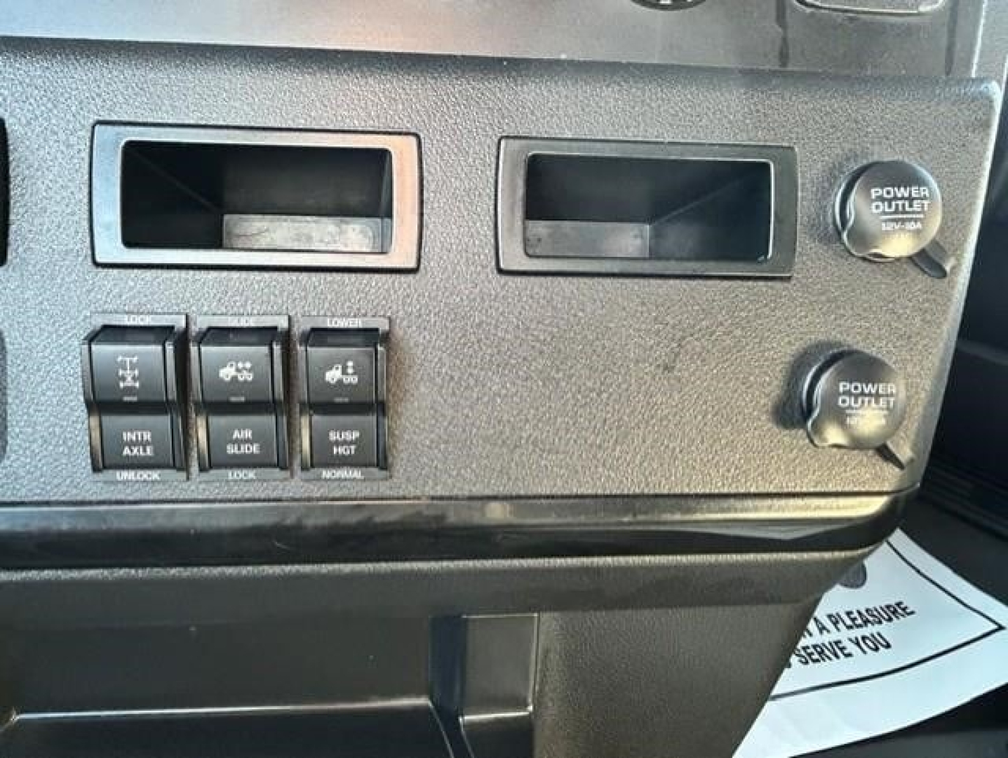 Dashboard area of 2023 Freightliner Cascadia 126 showing power outlets and control switches with labels such as INTR AXLE, AIR SLIDE, SUSP HOT, NORMAL, and window plenum.