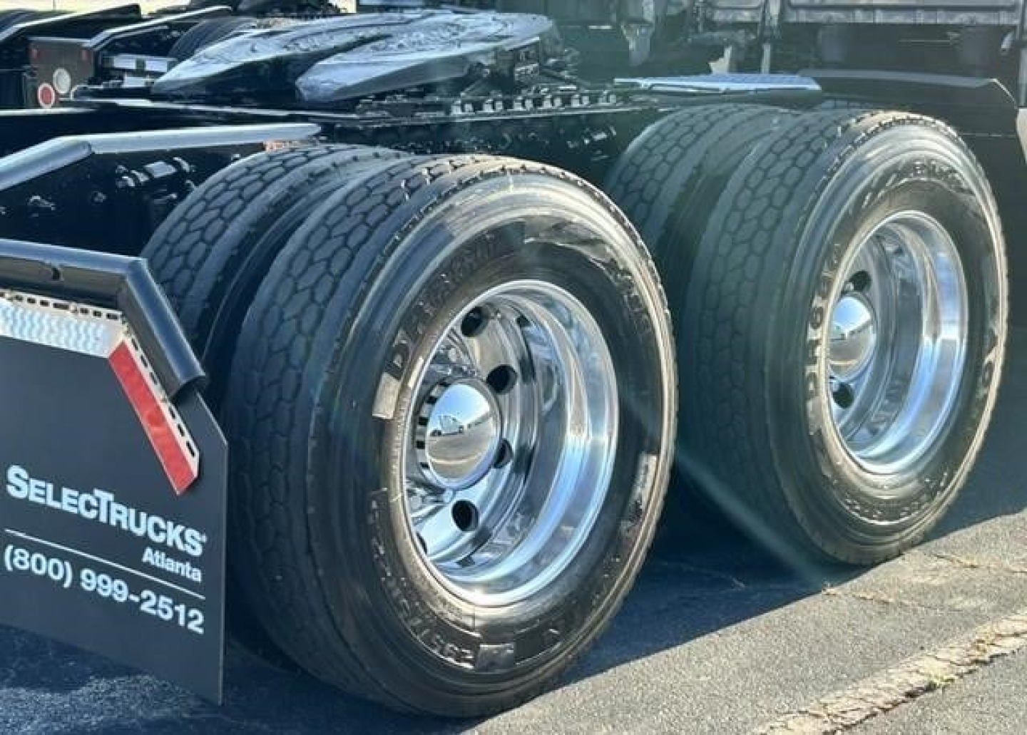 Freightliner Cascadia truck rear dual rear wheels showing tires and chrome rims, with SelectTrucks Atlanta mudflap and contact number.