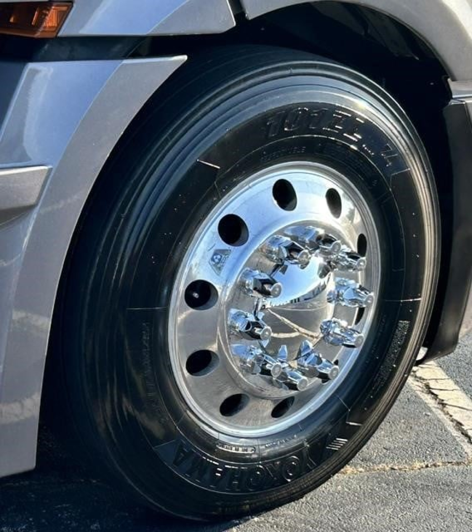 Truck front wheel close-up showing chrome polished hub, tire, and rim on Freightliner Cascadia 126. Visible tire sidewall branding and wheel lug nuts.