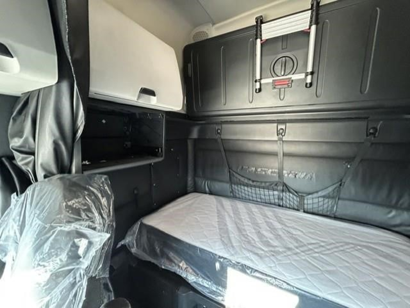 Truck sleeper cab interior showing bunk bed with protective plastic on seat and storage net, Freightliner Cascadia 126 interior