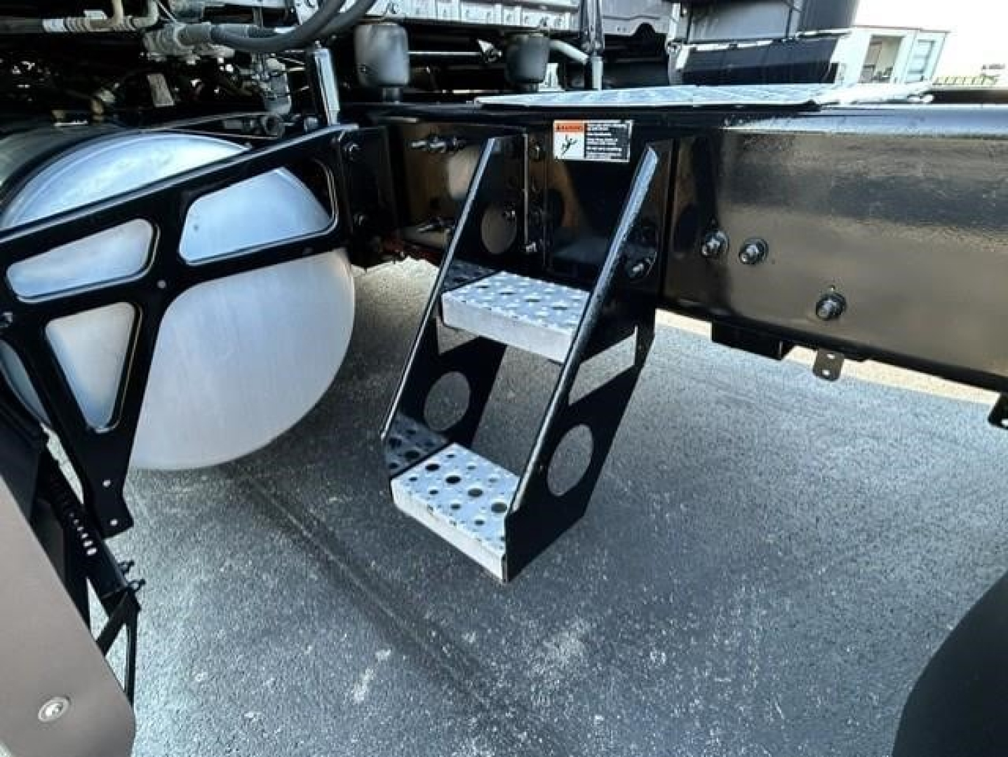 Step access ladder mounting under Freightliner Cascadia 126 truck chassis showing metal perforated steps and frame mounting points.