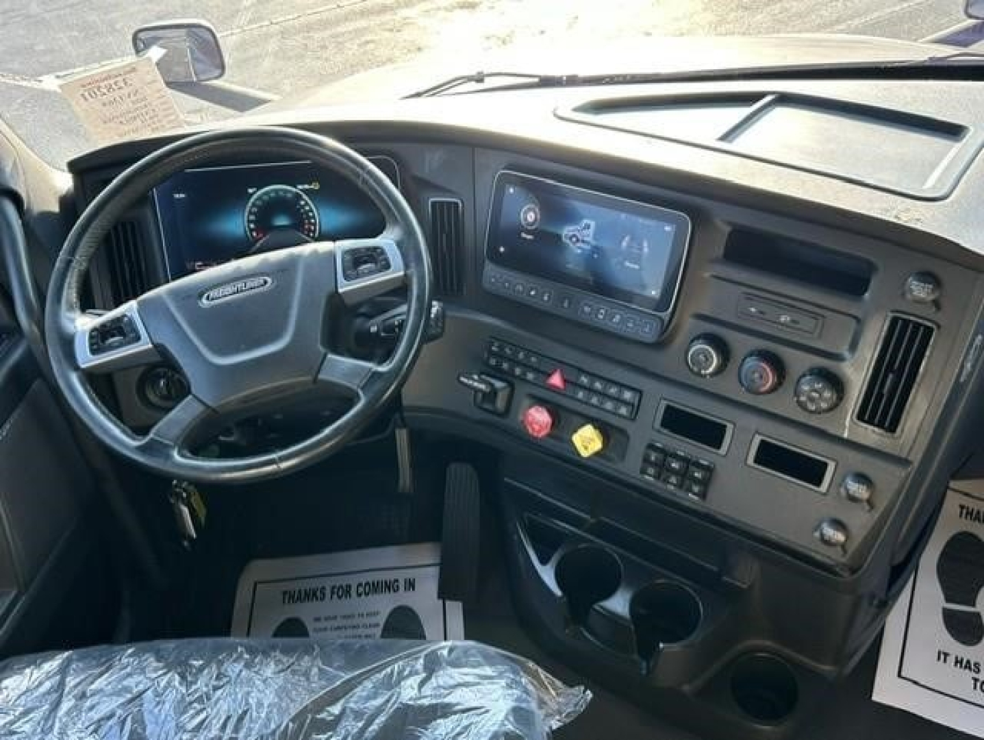 Freightliner Cascadia dash area showing steering wheel and dashboard with large central touchscreen display and control panel.
