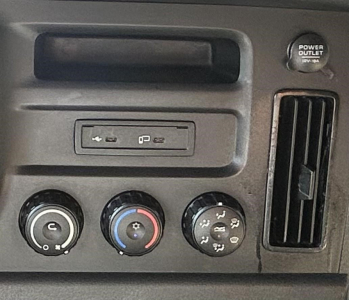 Freightliner Cascadia instrument panel showing HVAC controls and power outlet cover.