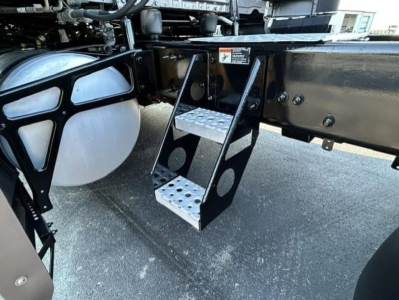 Step access ladder mounting under Freightliner Cascadia 126 truck chassis showing metal perforated steps and frame mounting points.