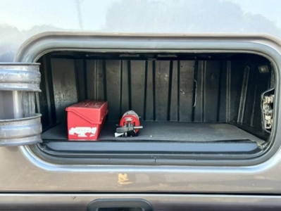 Truck cab storage compartment showing a red battery box and a small red tool pouch, with a black interior.