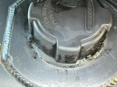 Fuel cap area with warning and oil fill markings on the tank; circular cap with embossed text around it: 'OPEN', 'TANK', 'FILL', 'WARNING' and other maintenance stamps.