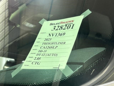 Truck with pink information tag on windshield showing stock number 328201, VIN NV1369, model CA126SLP, DD-15 engine, DT-12 automatic, 2.85 rocker ratio, CTG frame.
