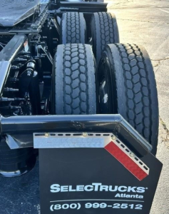 Trailer/tractor rear showing dual rear axles and tires, SelectTrucks Atlanta plate, rear fender/step with red reflector and metal perforated trim, partial drive line components.