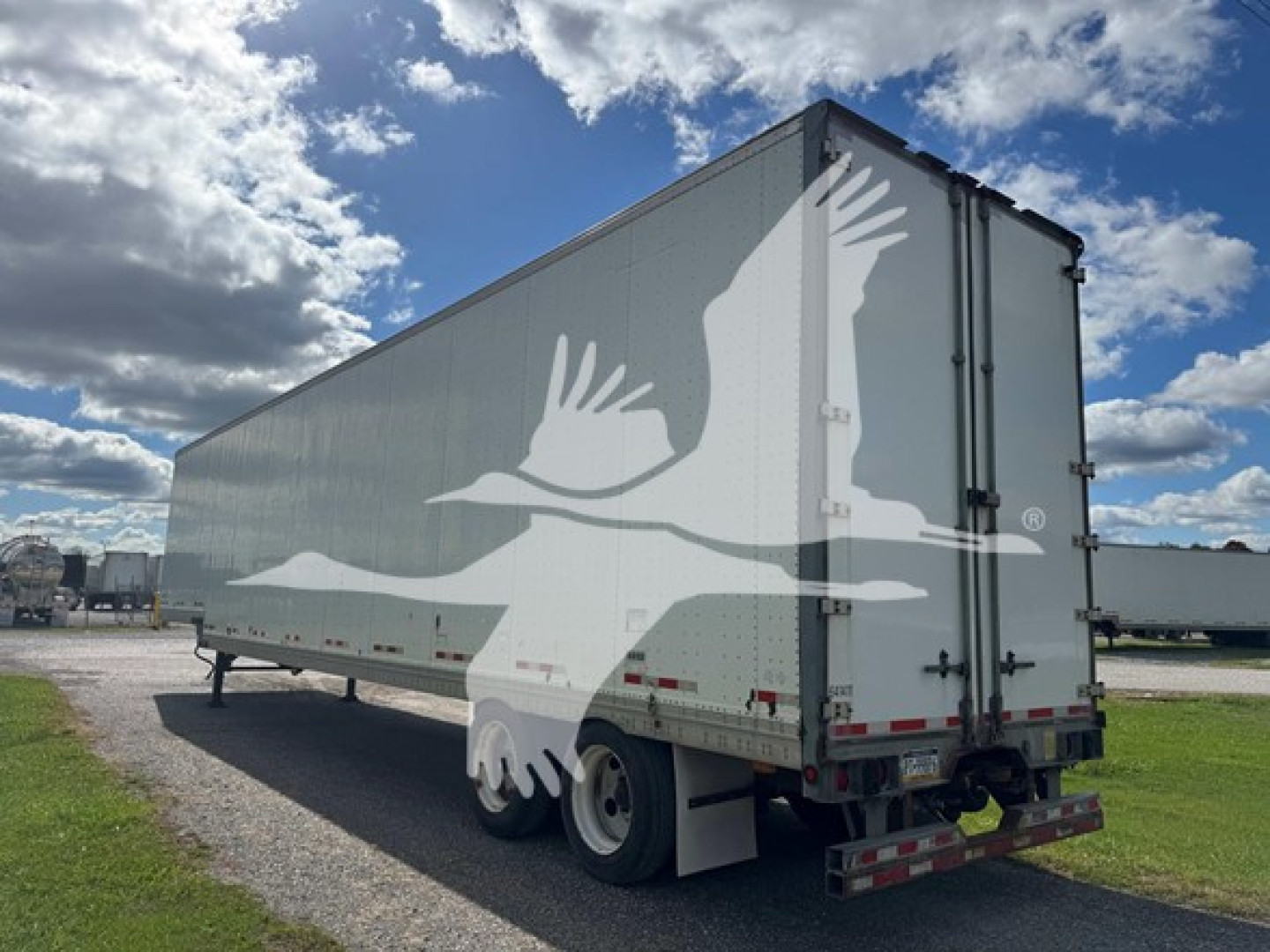 Manac drop van trailer showing side and rear views with a large white bird graphic on gray walls.