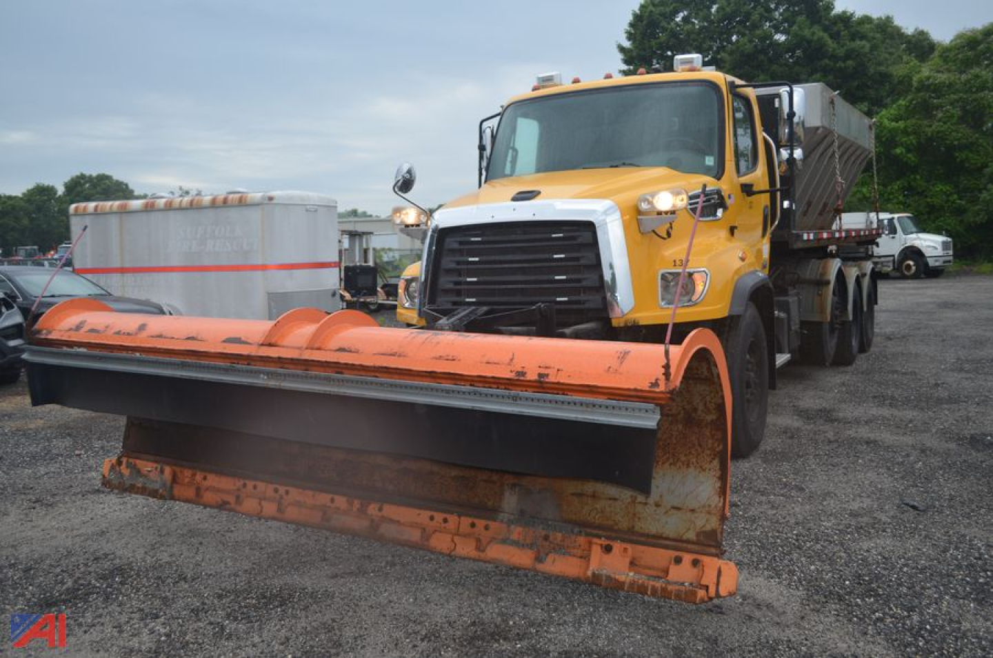 Front view of a yellow Freightliner 114 SD with an orange snow plow attached, heavy-duty truck in a lot.