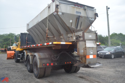 Truck rear view showing a Freightliner 114 SD sander with plow attachments and dump bed, dual rear axles, gray metal hopper, and towing setup.