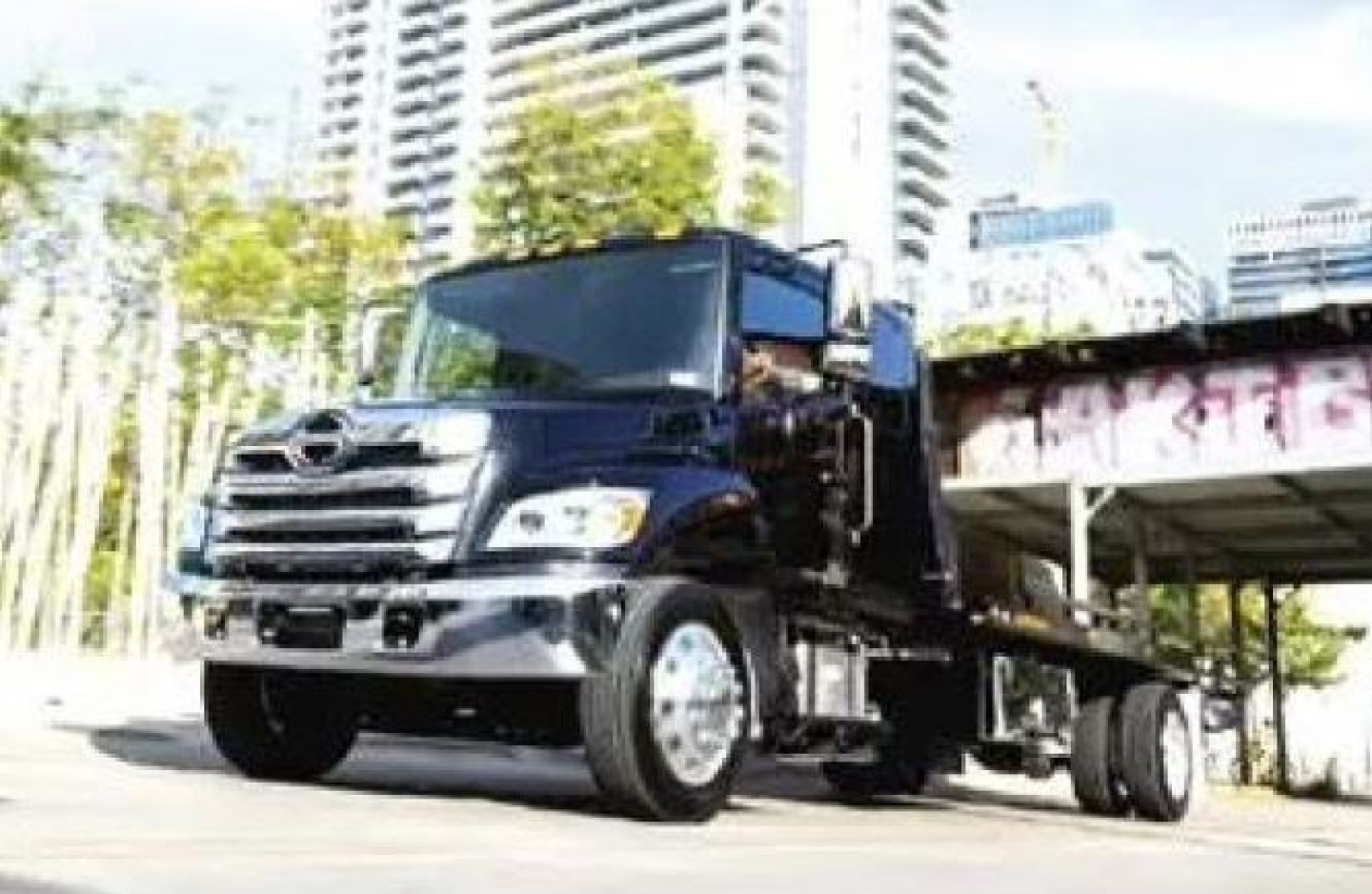 Truck cab and chassis showing 2027 Hino L7 with black paint, front grille, and left-side view.