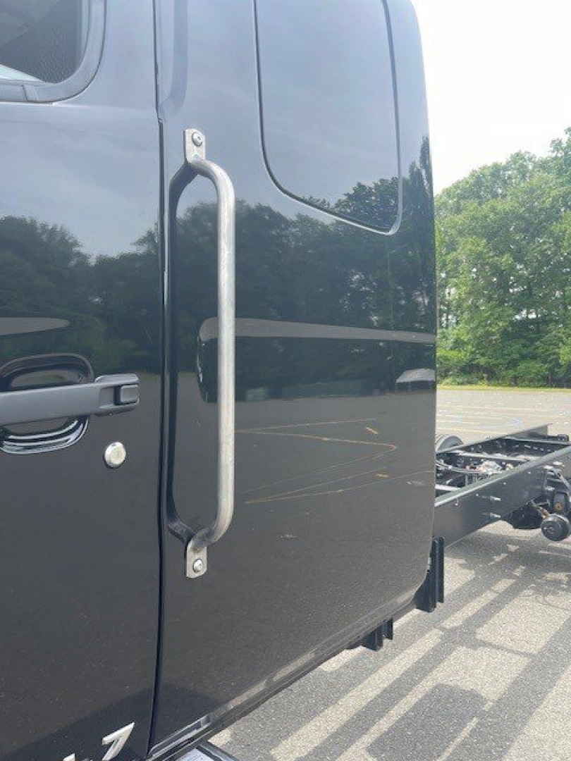 Truck door with large vertical grab handle on a dark cab, partial hitch frame visible at rear, no cab roof details.